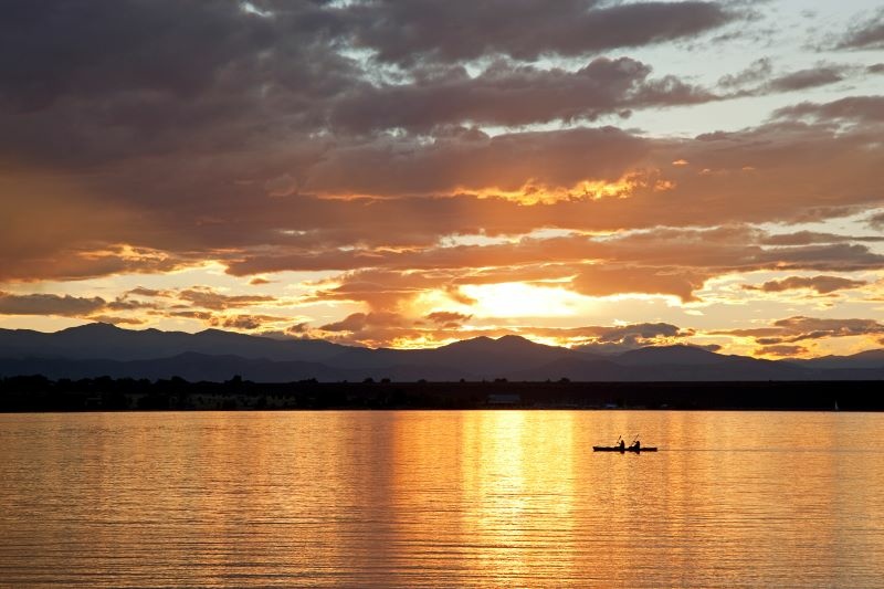 Cherry Creek State Park. Sunset behind mountains, canoe paddling acrossstilllake